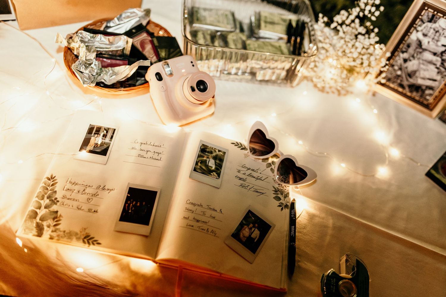 Wedding guestbook display with vintage photos, flowers and decorative lighting.