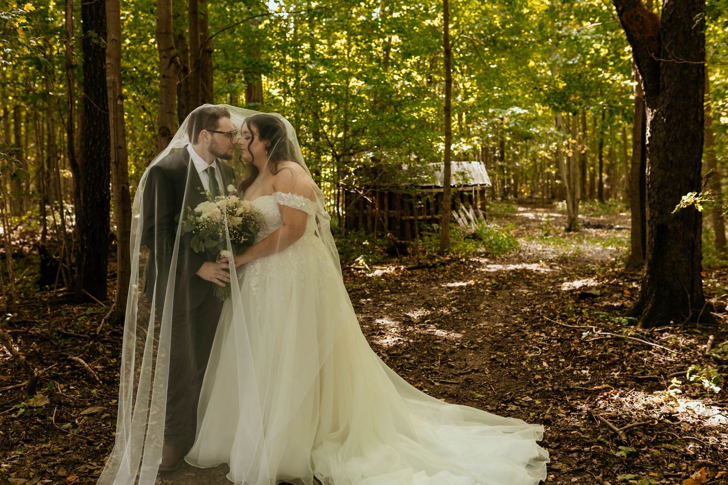 A romantic outdoor wedding photo session in a sunlit wooded area with a flowing white dress creating an ethereal scene.
