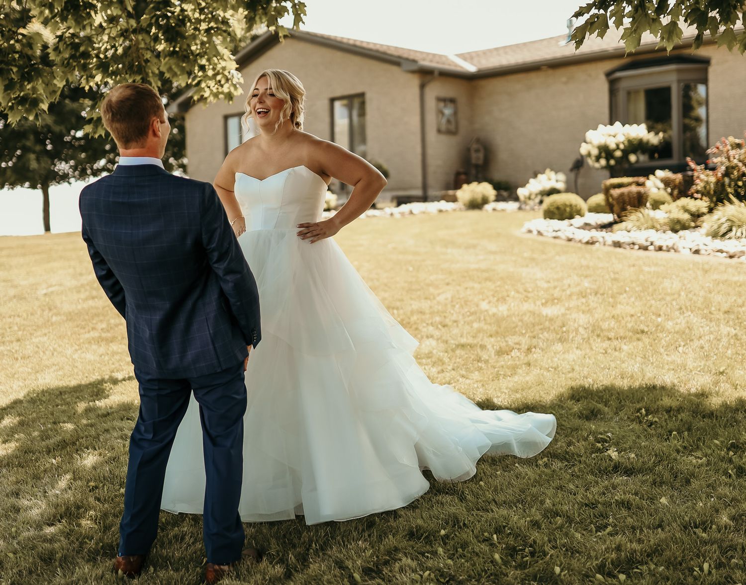 Elegant outdoor wedding scene with couple in navy suit and flowing white gown on sunny lawn.