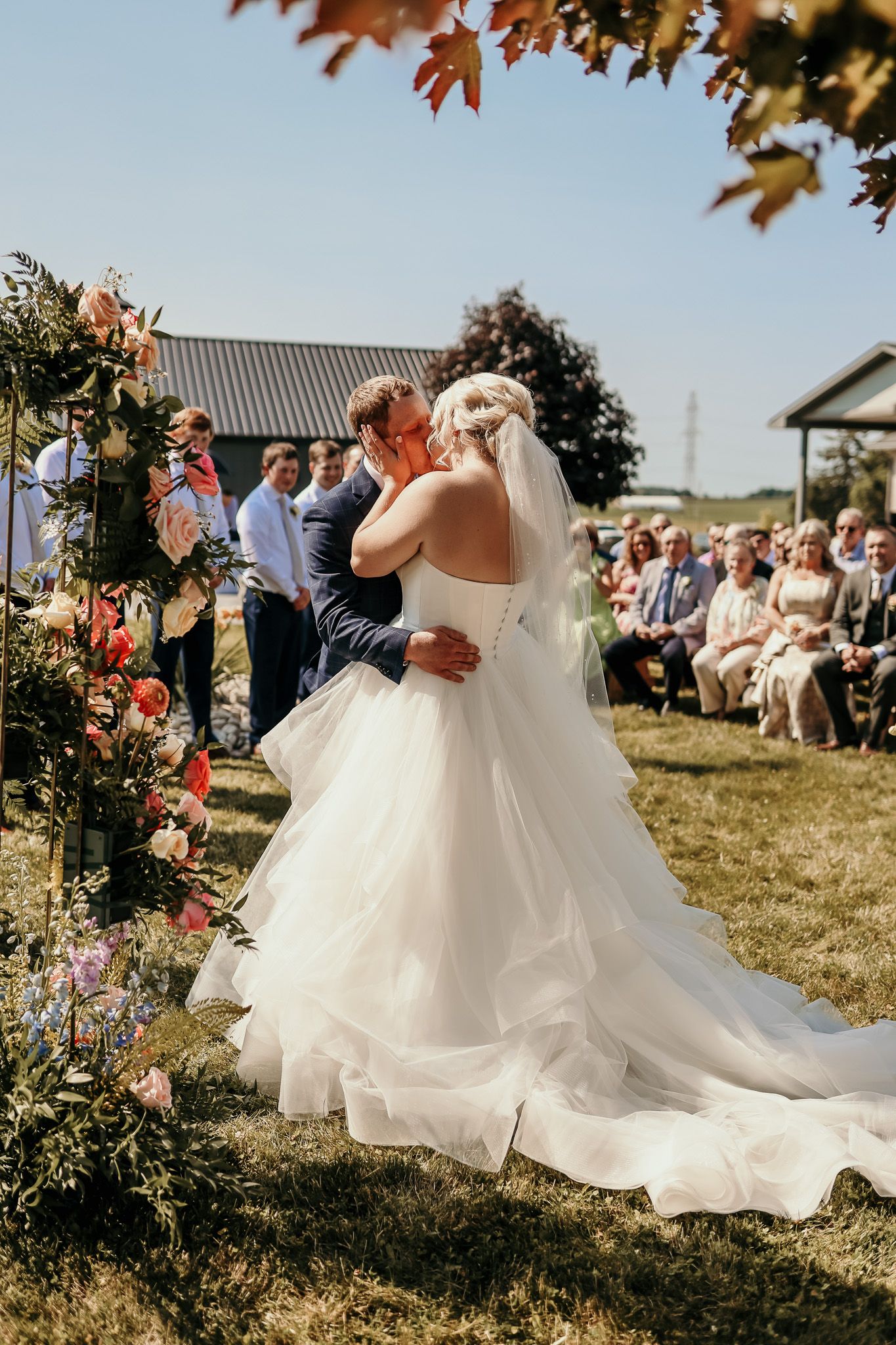 Garden wedding ceremony with floral arch and guests viewing couple's first kiss.