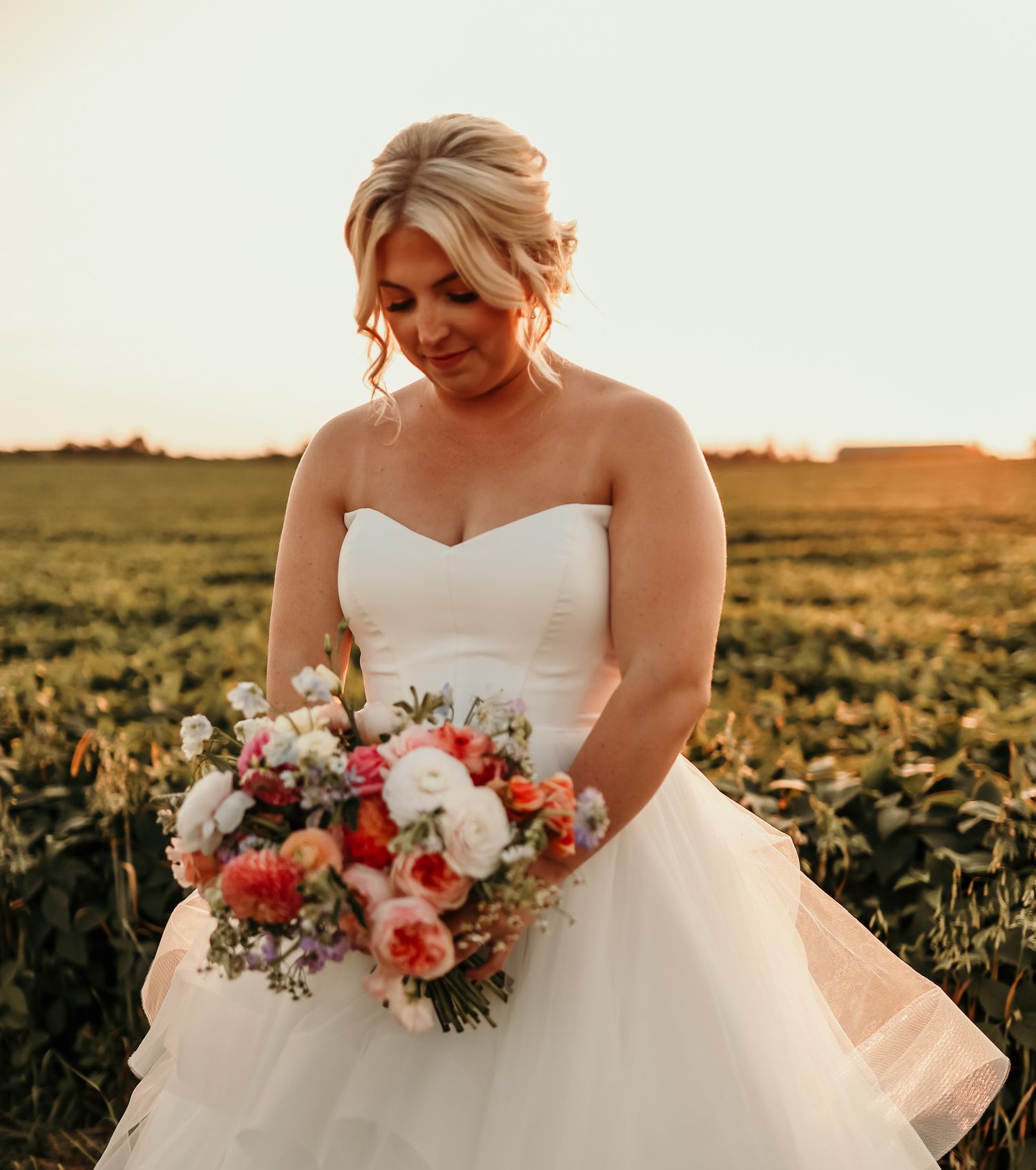Sunset bridal portrait featuring white strapless gown and colorful bouquet in field.