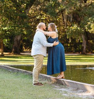 A couple shares an intimate moment while standing on the edge of a reflecting pool in a park.