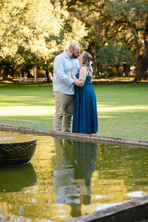 A couple embraces on the edge of a reflecting pool during golden hour in a park setting.