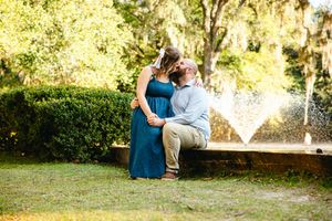 A couple sits together on a bench with a fountain spraying water in the background.