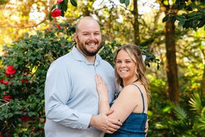 A couple poses together in front of blooming red camellias in a garden setting.