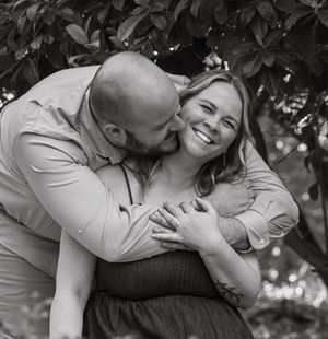 A black and white portrait of a couple sharing an intimate embrace outdoors.