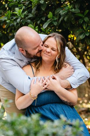 A couple shares a tender moment among green foliage in natural lighting.
