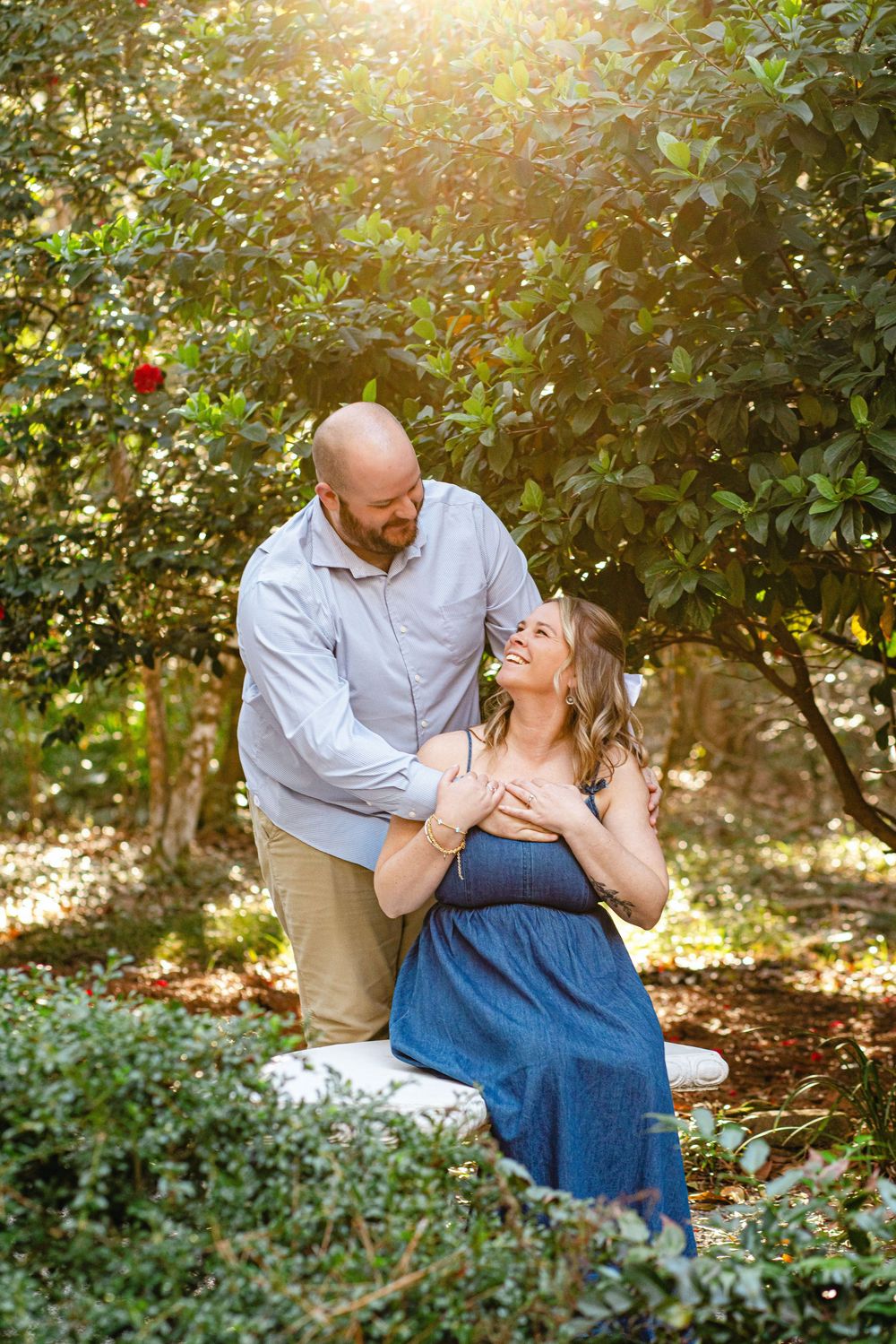A couple shares a romantic moment in a garden with golden sunlight filtering through trees.