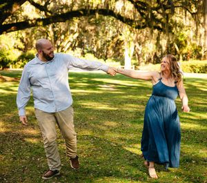 A couple shares a romantic moment in a sunlit park with Spanish moss draped trees.