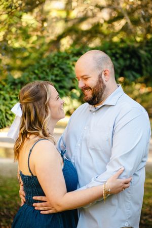 A couple embraces and laughs together in a sun-dappled outdoor setting.