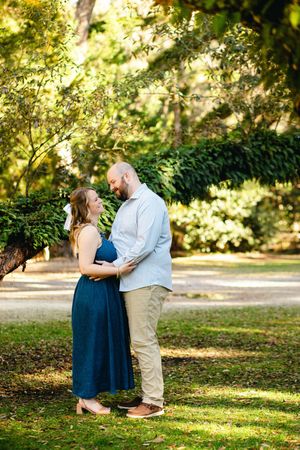 A romantic moment captured in a park with dappled sunlight and green foliage.