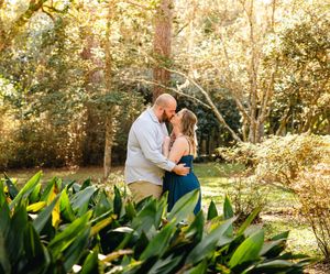 A romantic scene unfolds in a garden setting with lush tropical plants and golden sunlight.