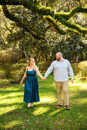 A couple shares playful moments in a park with Spanish moss hanging from trees.