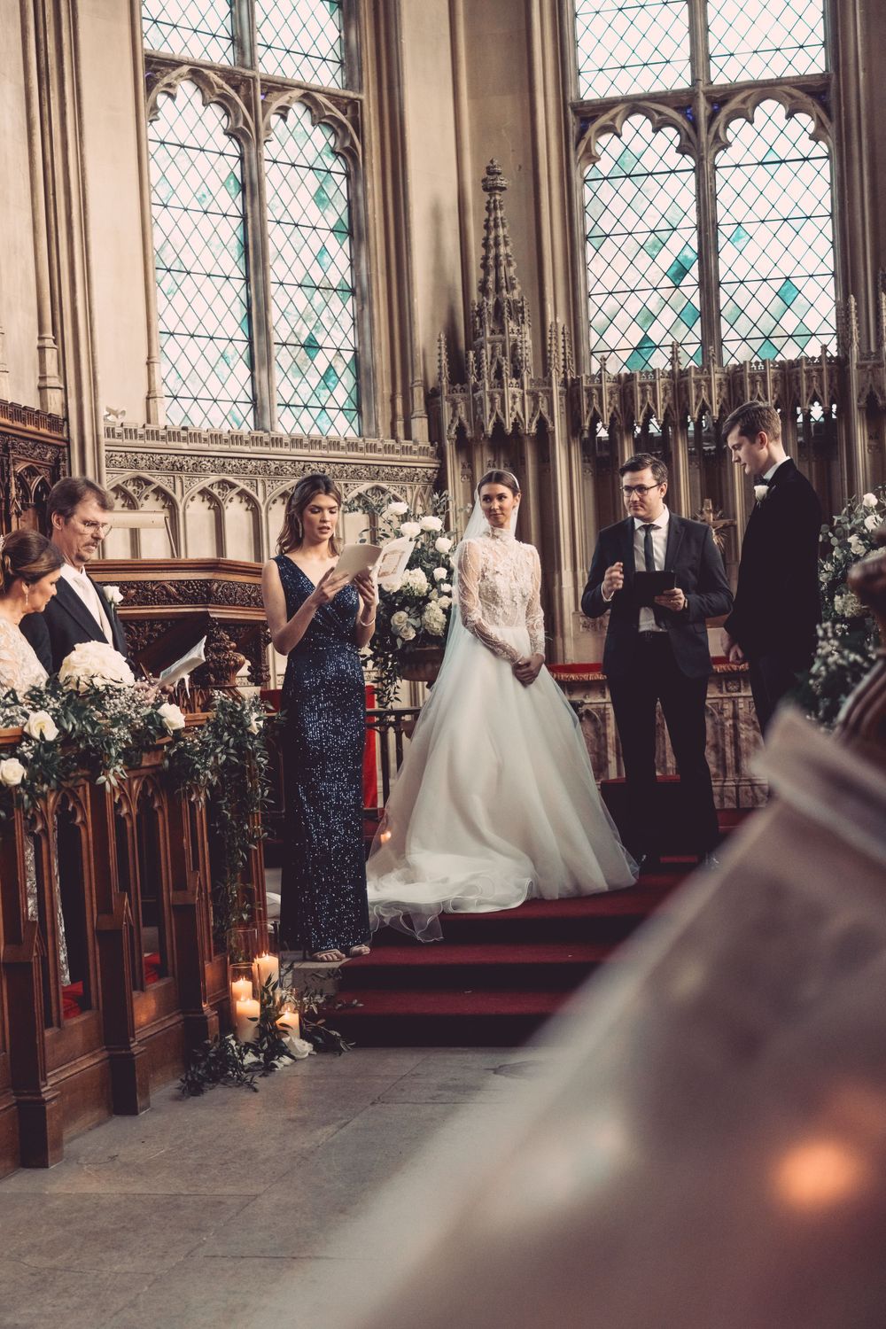 Wedding ceremony in progress inside historic church with gothic windows and candlelit details at Ashridge House.