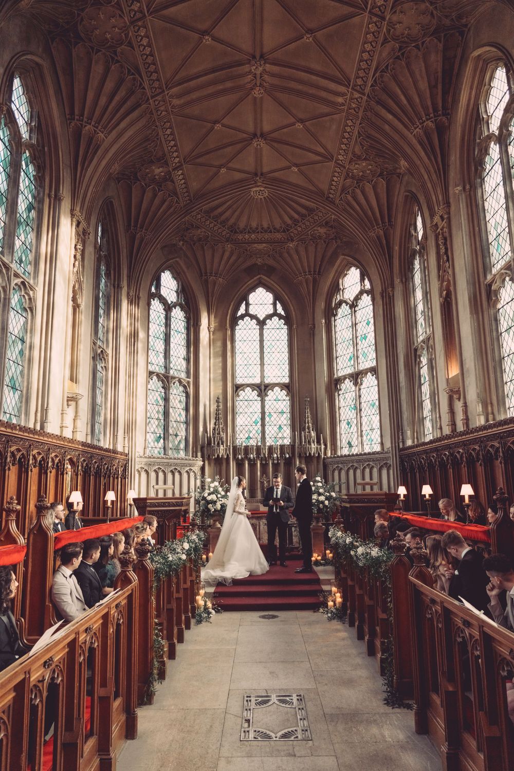 A grand church wedding ceremony viewed from above showing vaulted ceilings and stained glass windows at Ashridge House.