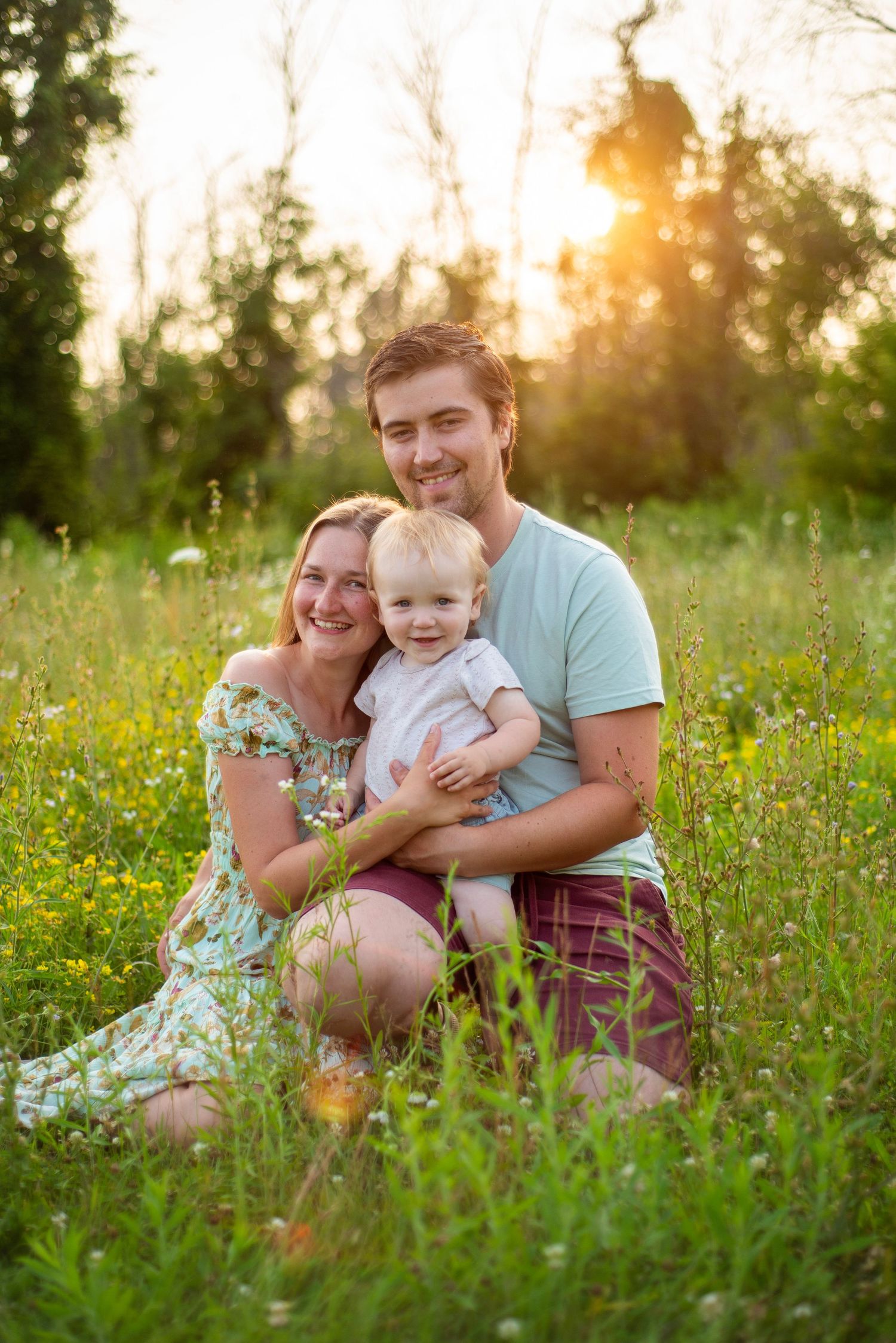 A family of three poses together in a wildflower meadow during golden hour.