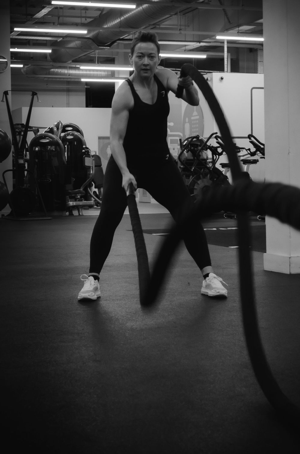 An athlete works out with battle ropes in a well-equipped modern gym facility.