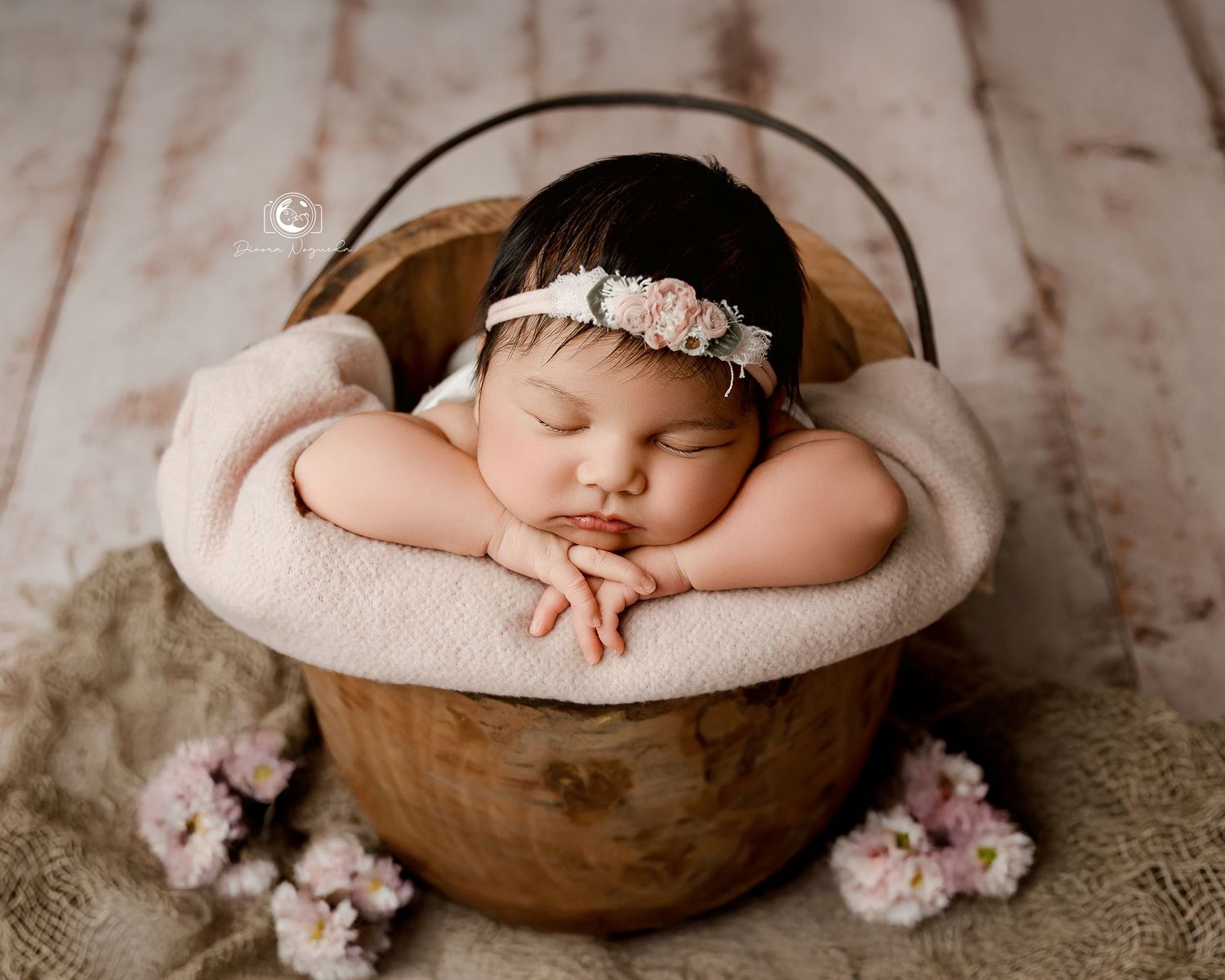 Newborn baby sleeping peacefully in white lace outfit against brown backdrop.