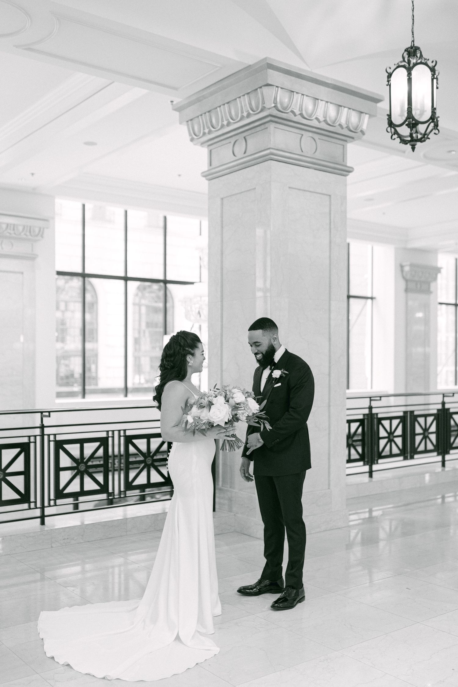 A romantic black and white wedding photo in an elegant venue with marble columns.
