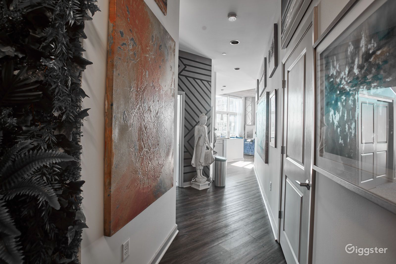 Modern art-filled hallway with hardwood floors, large paintings, and a sculpture near bright windows.