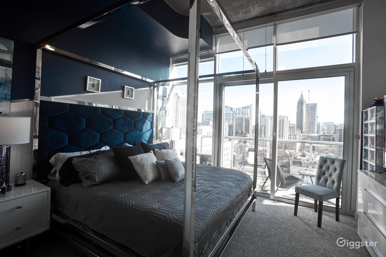 Luxurious blue-themed bedroom with a canopy bed and floor-to-ceiling windows overlooking a city skyline.
