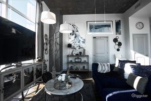 Stylish modern living room with navy blue sofa, marble coffee table, large windows, and abstract wall art in a luxury loft.