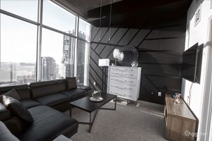 Modern loft bedroom with black geometric accent wall, large city-view windows, sectional sofa, and contemporary decor.