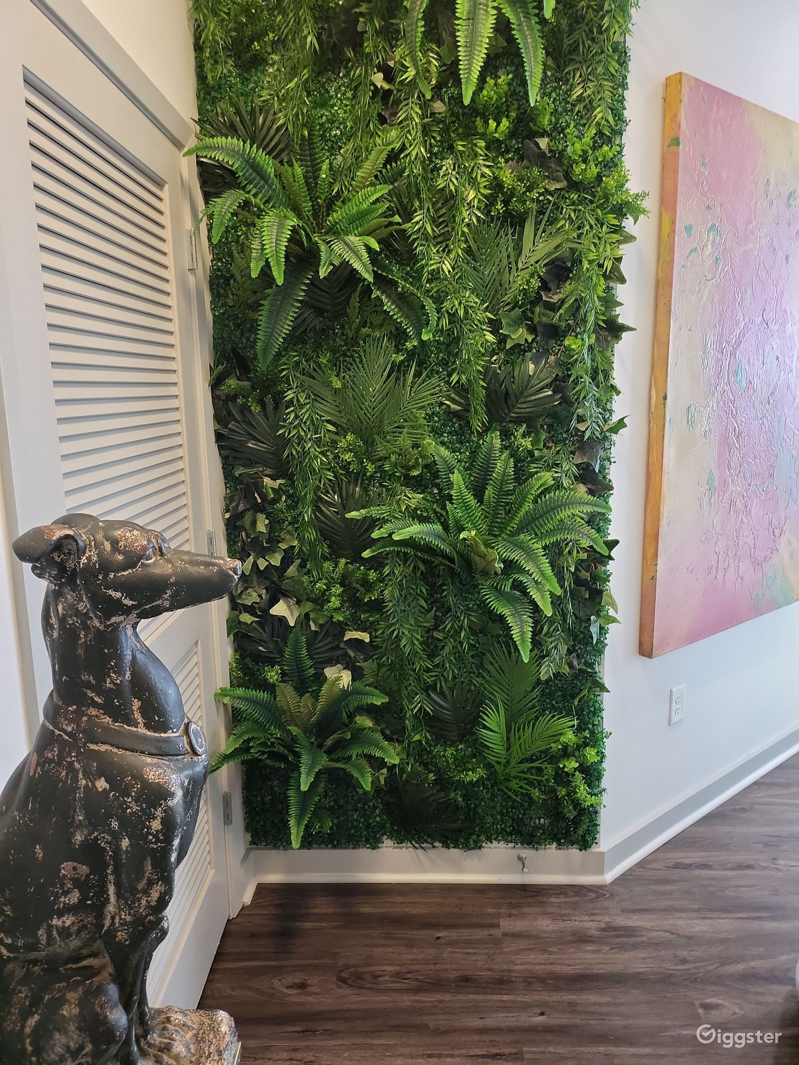 Dramatic indoor vertical garden wall with lush tropical ferns beside a decorative horse sculpture and pink canvas art.