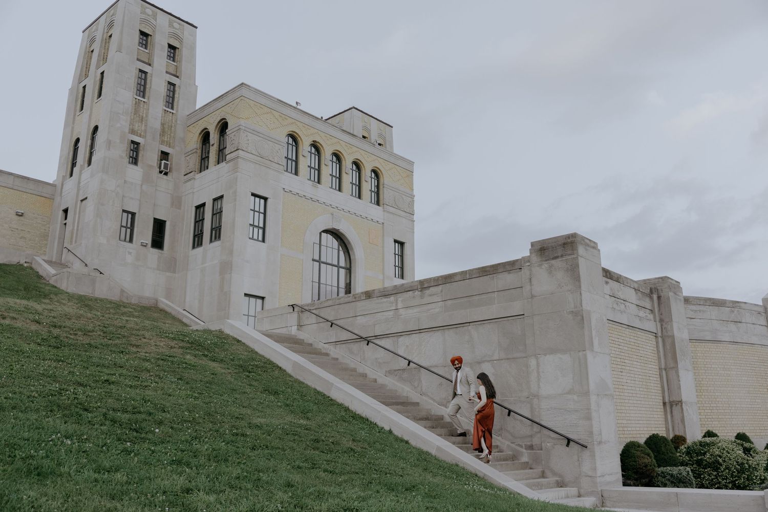 A couple ascending white stone stairs of an Art Deco style building with tower architecture.