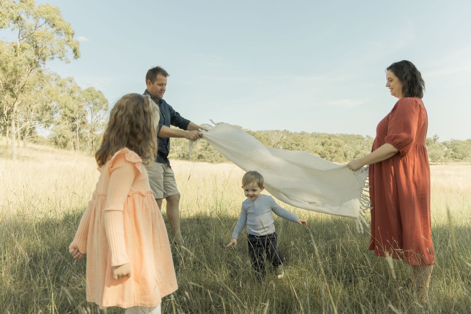 Family playing with white fabric in a sunny field creating joyful moments together.
