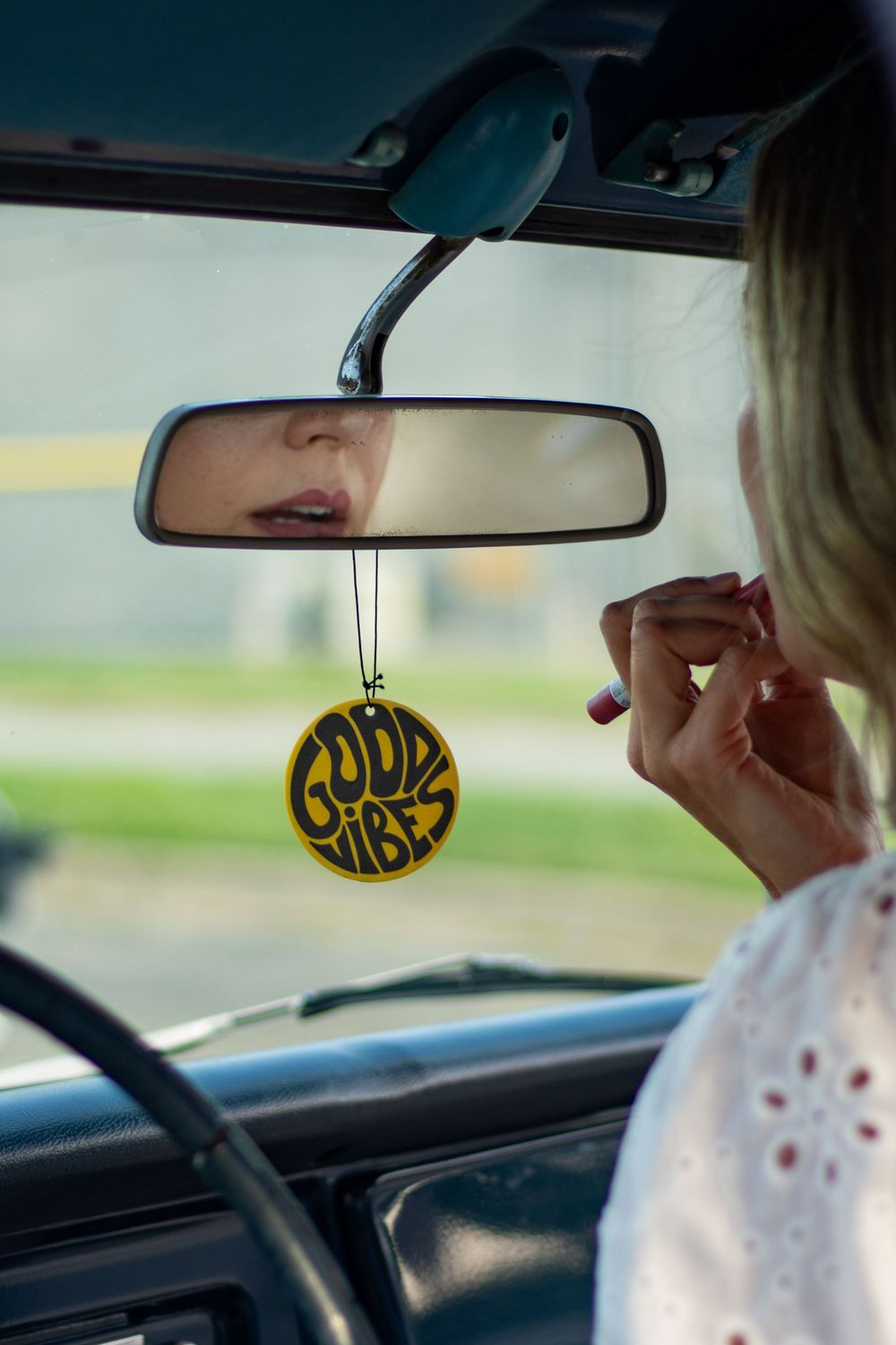 Yellow 'Good Vibes' car air freshener hanging from rearview mirror.