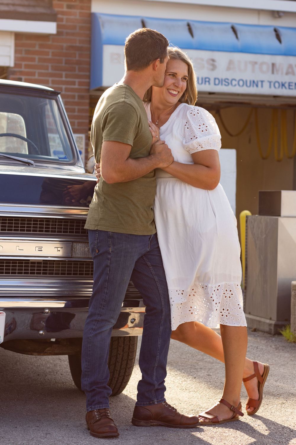 Couple embracing near vintage car outside brick building.
