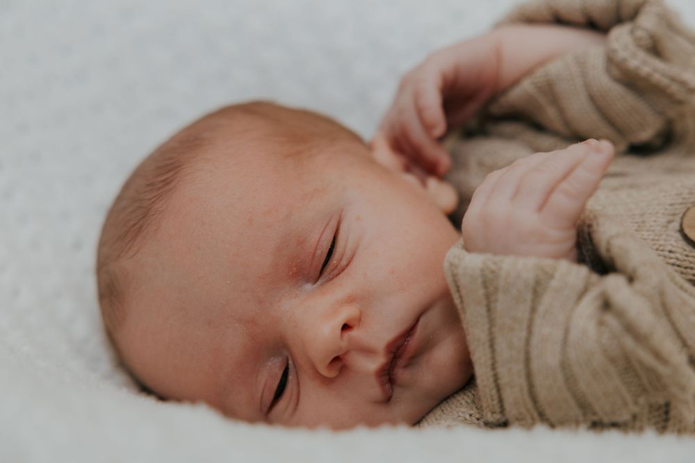 Peaceful sleeping baby wearing beige knit sweater on white surface.
