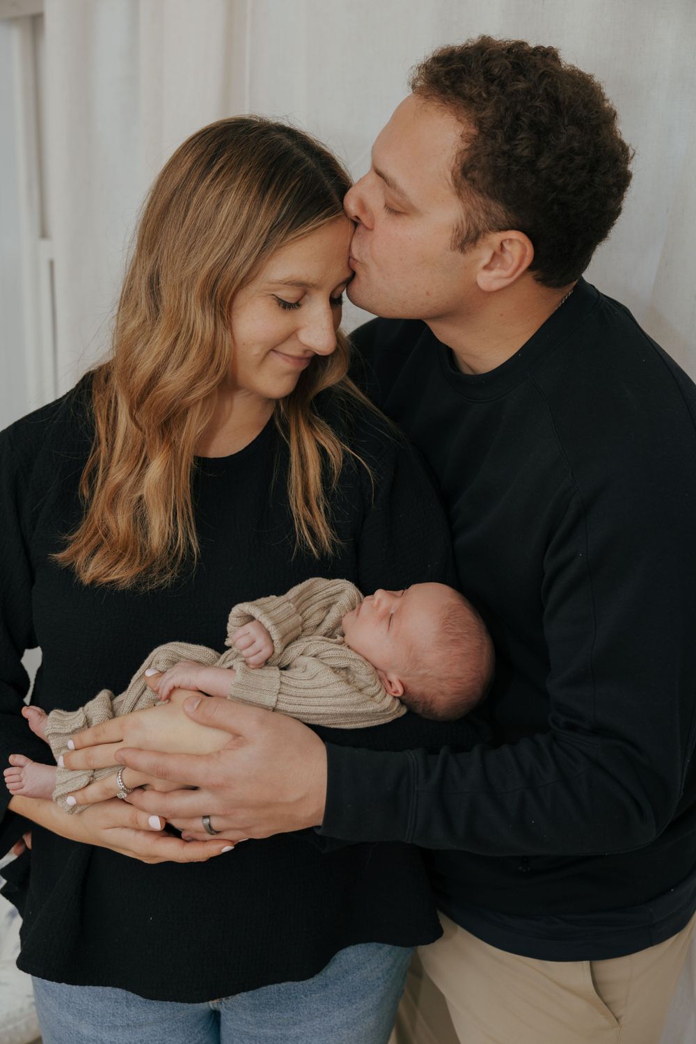 Gentle family moment with sleeping newborn in knit sweater.