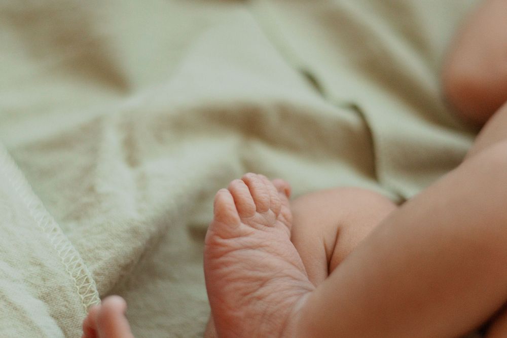 Delicate detail of a newborn's tiny foot resting on cream-colored fabric.
