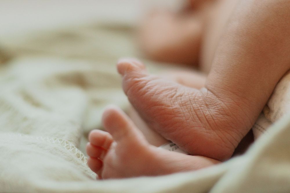 Soft focus image of a newborn's feet against light-colored bedding.