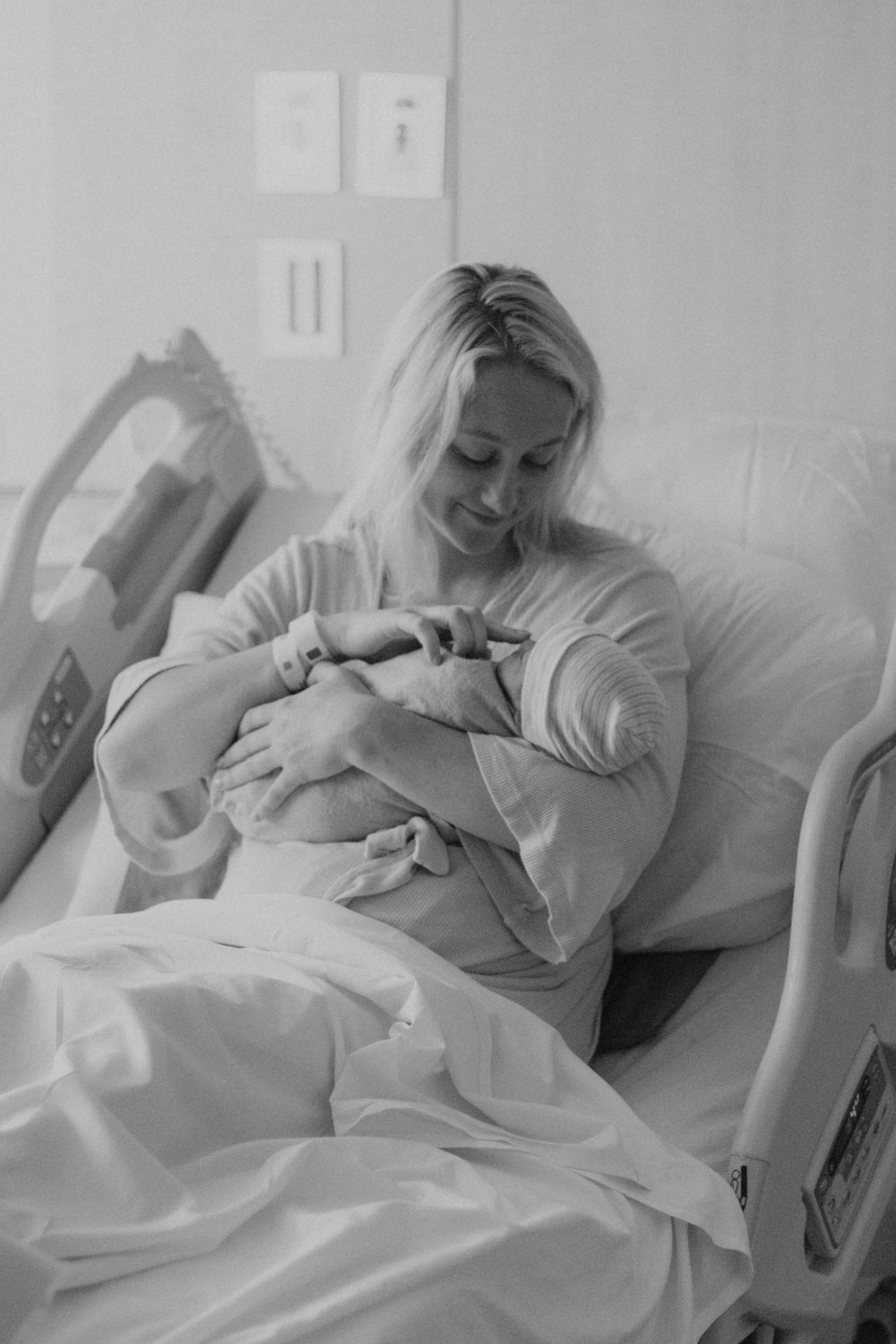 Black and white image shows tender moment in hospital room with newborn.