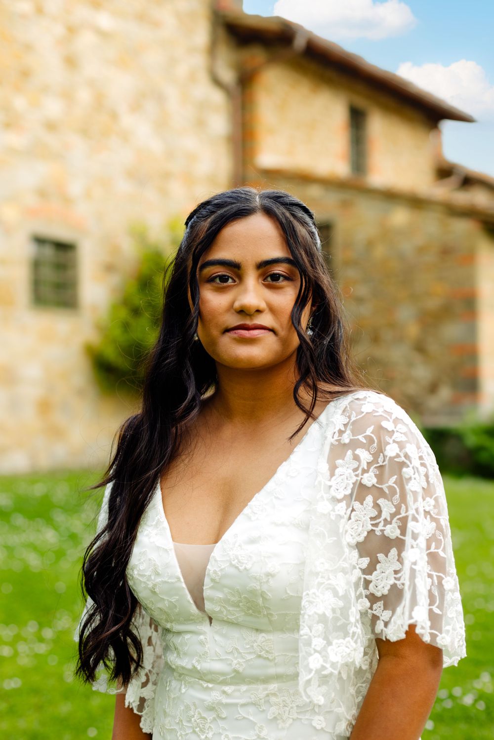 Close-up shot of bride in lace flutter sleeve wedding dress against stone building.