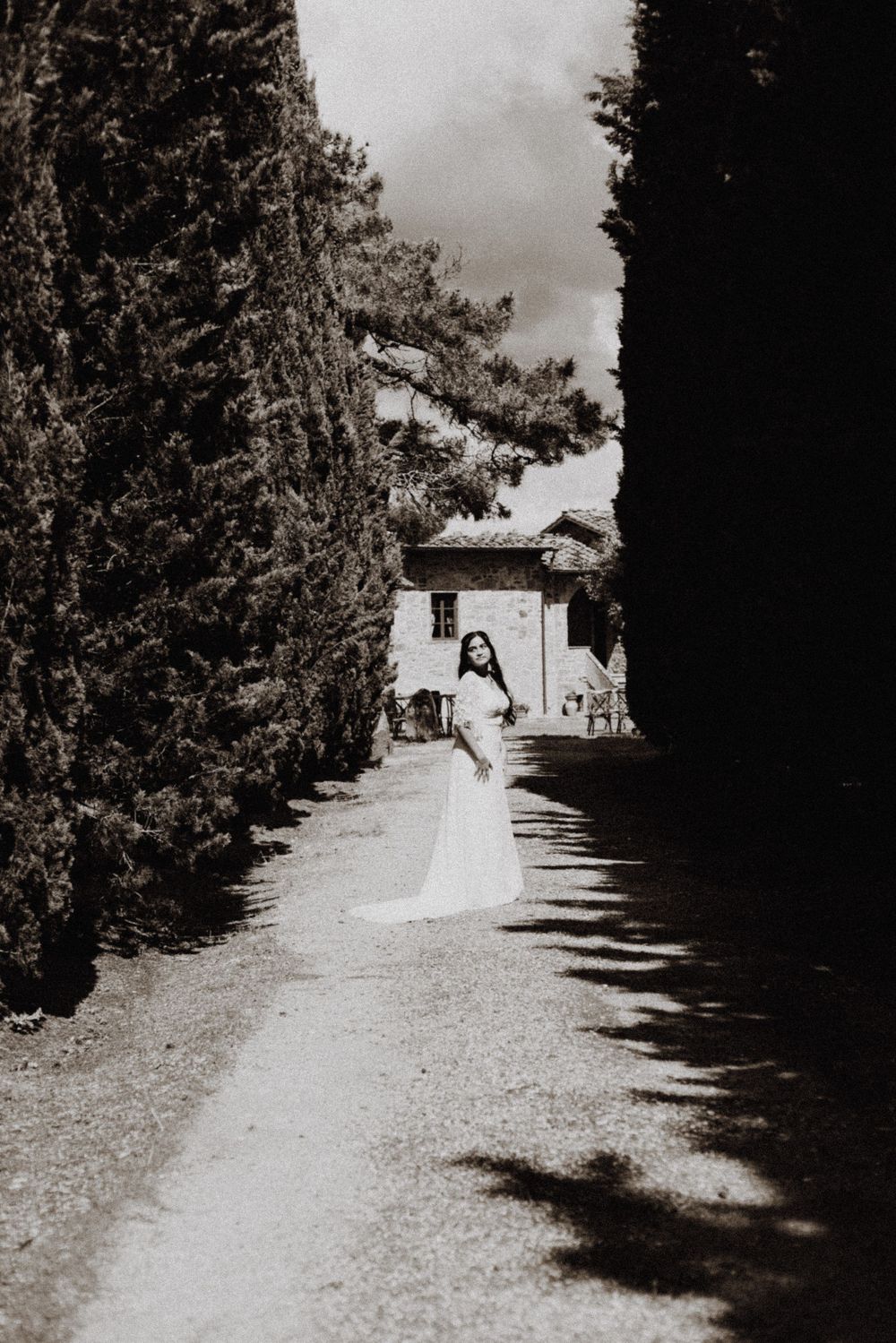 A series of black and white wedding photos showing someone in a white dress walking along a garden path.