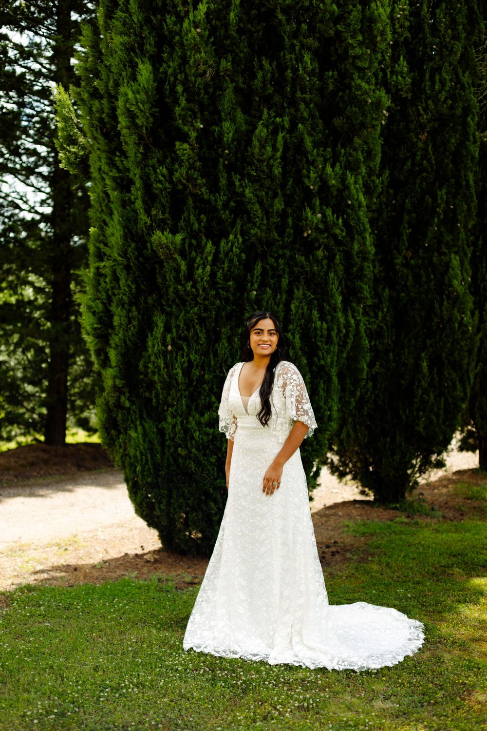 Wedding photos in a garden setting with cypress trees and white dress details.