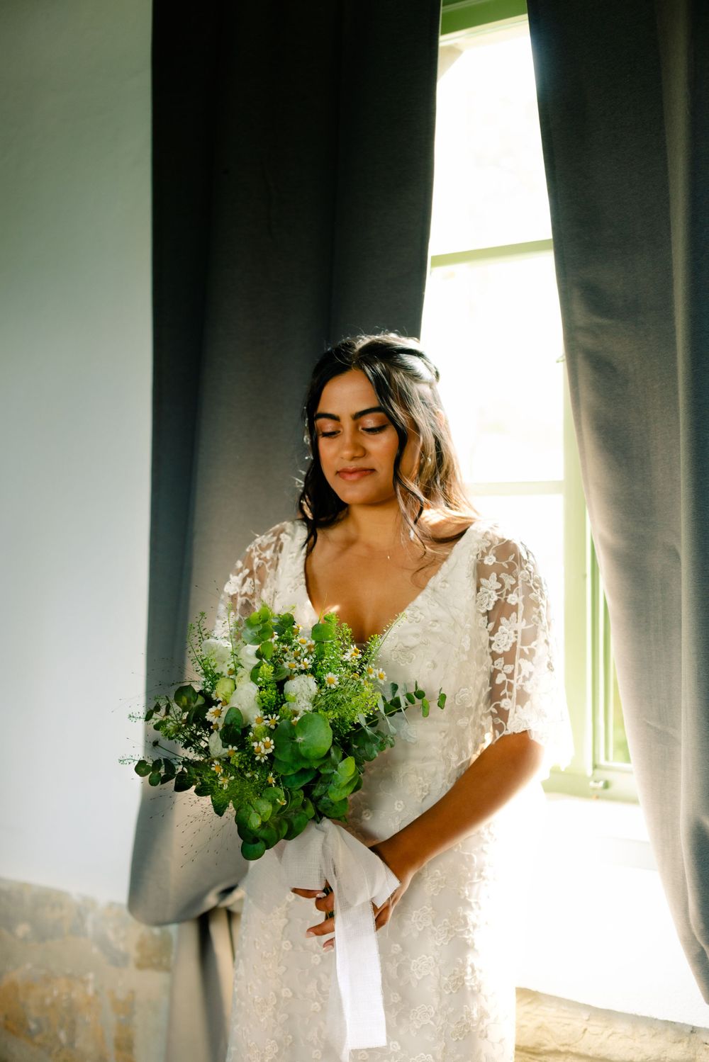 Dramatic window-lit photos with a white bouquet and lace wedding dress.