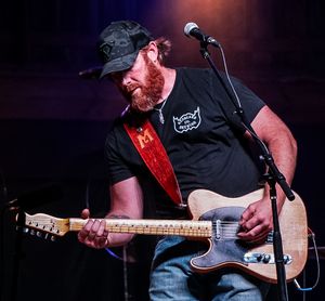 Musician performing on stage with guitar under dramatic concert lighting.