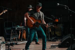 Country musicians performing with acoustic guitars on a dimly lit stage.