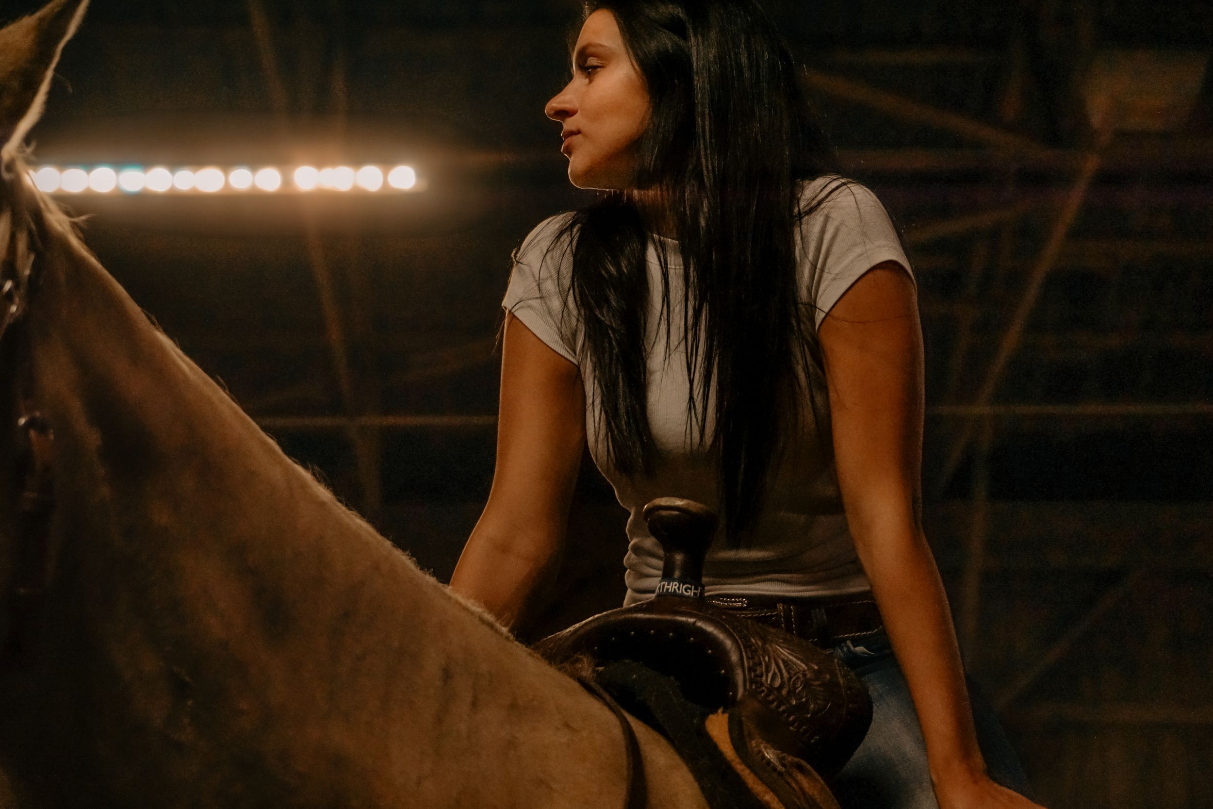 Rider sits astride a horse in a dimly lit indoor arena.
