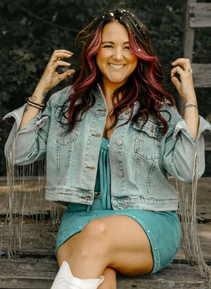 Casual portrait of someone with vibrant hair wearing denim jacket sitting outdoors.