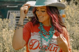 Western style portrait with turquoise jewelry and vintage graphic tee in sunlit field.