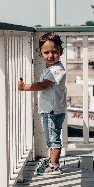 Small child in casual wear standing against white railings on a deck.