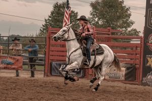 A rider in western attire races a white horse through a rodeo arena.
