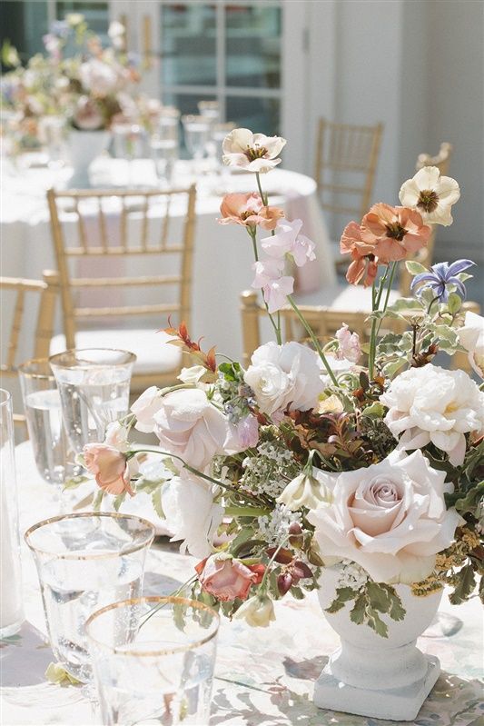 Elegant wedding table setting with pastel floral centerpiece featuring roses and poppies in a white vase with crystal glassware.