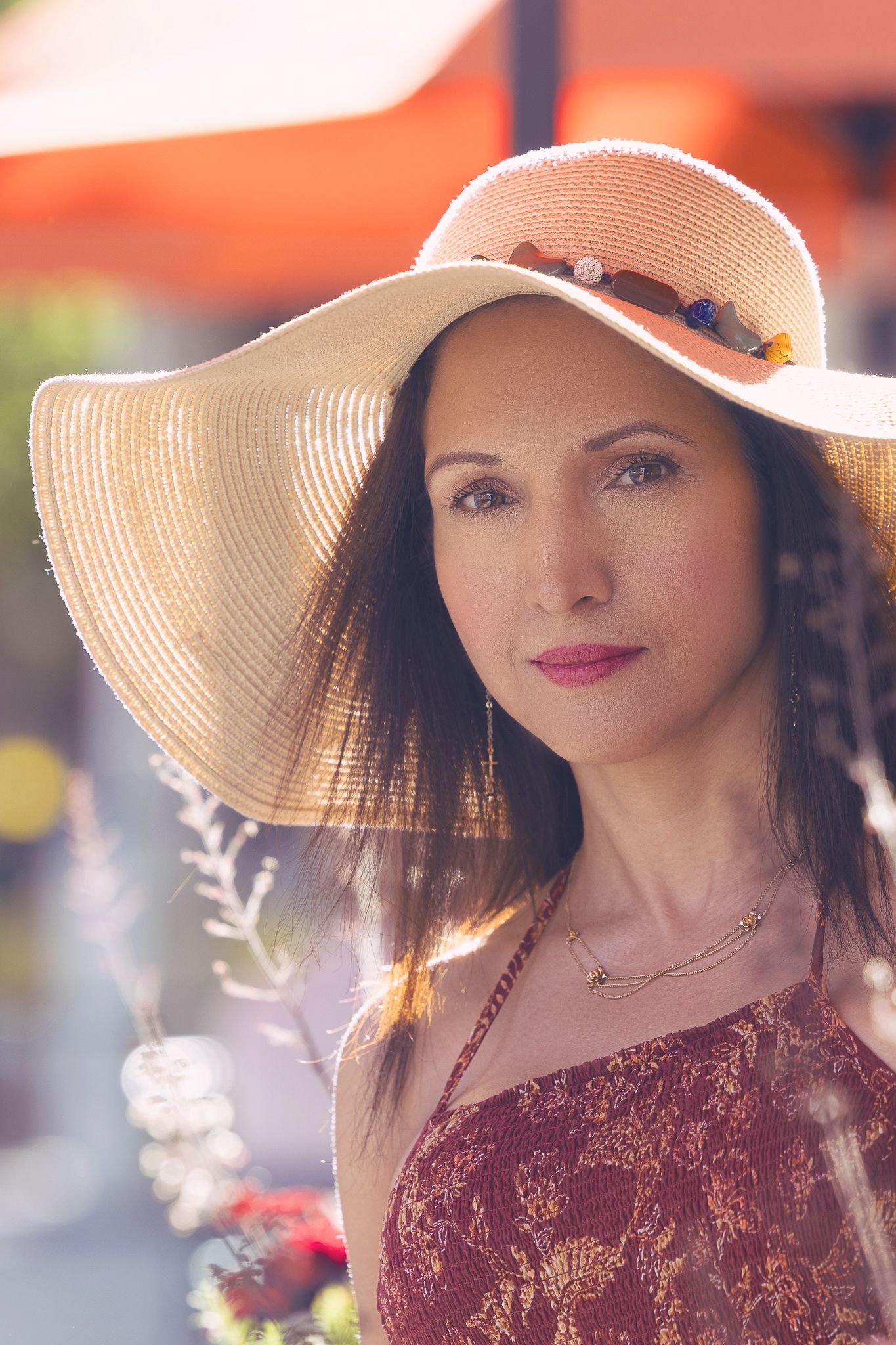 Someone wearing a beige sun hat and burgundy lace dress poses outdoors on a sunny day.